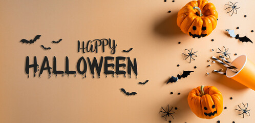 Halloween decorations made from pumpkin, paper bats and black spider on pastel orange background. Flat lay, top view with Happy Halloween text.
