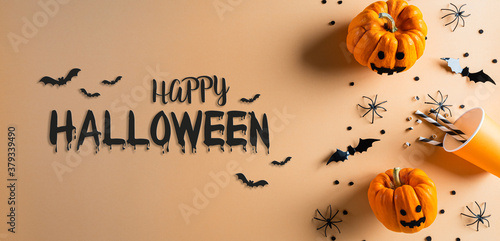 Halloween decorations made from pumpkin, paper bats and black spider on pastel orange background. Flat lay, top view with Happy Halloween text.