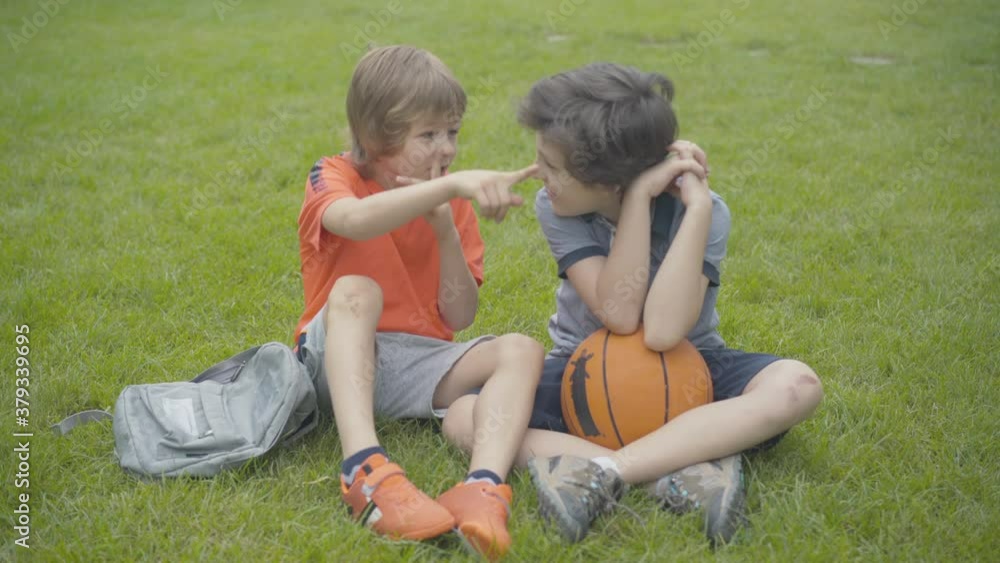 Cheerful Caucasian boys sharing secrets outdoors. Portrait of joyful friends or brothers talking, giving high five, and laughing. Friendly siblings resting in park. Cheerful Caucasian boys sharing secrets outdoors. Portrait of joyful friends or brothers talking, giving high five, and laughing. Friendly siblings resting in park.