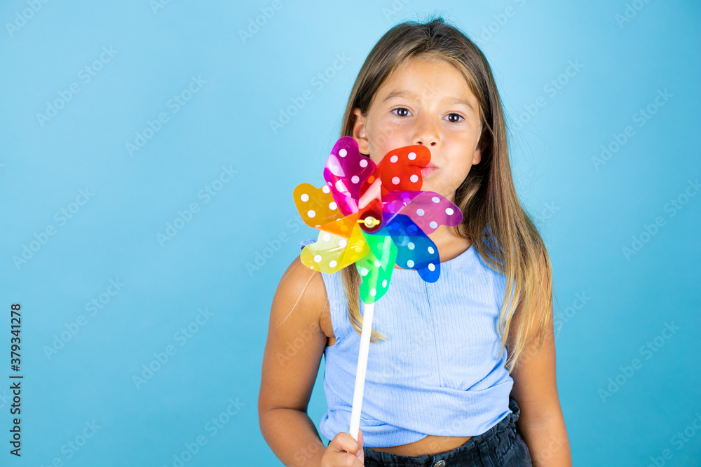 Young beautiful child girl over isolated blue background blowing a pinwheel Young beautiful child girl over isolated blue background blowing a pinwheel