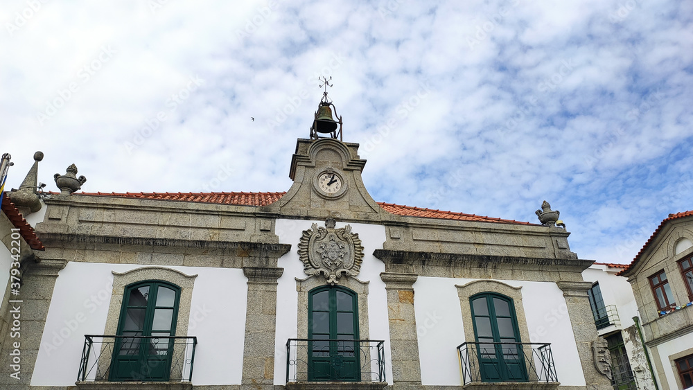 The facade of the City Hall of Esposende, district of Braga in Portugal. The window-balcony and the baroque carvings of weapons framed by a small bell tower equipped with a clock.