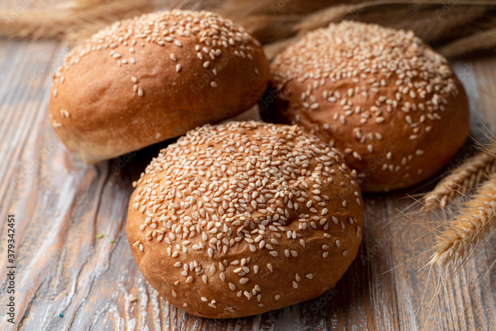 Simple wheat buns with sesame, on a rustic wooden table with spikes around