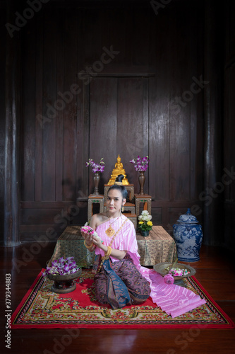 Pretty portrait Asian Thai woman sit with beautiful garland in here hand and wearing traditional Thai dress costume according Thai culture at ancient house in Ayutthaya, Thailand