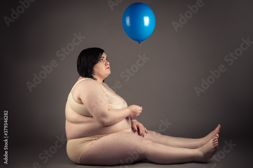 attractive fat woman sitting on the floor with blue balloon in hands