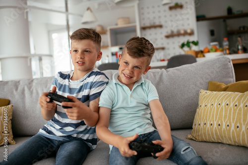 Happy brothers playing video games. Young brothers having fun while playing video games in living room.