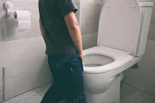 The boy is peeing into the toilet bowl in the restroom