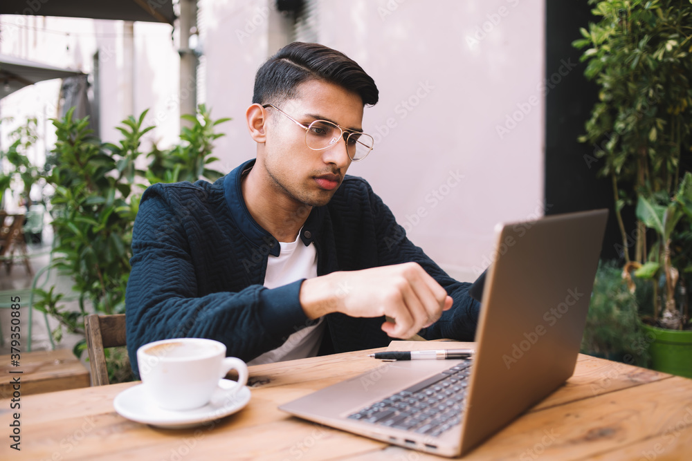 Young man using laptop and taking notes while enjoying coffee in cafe outdoors Young man using laptop and taking notes while enjoying coffee in cafe outdoors