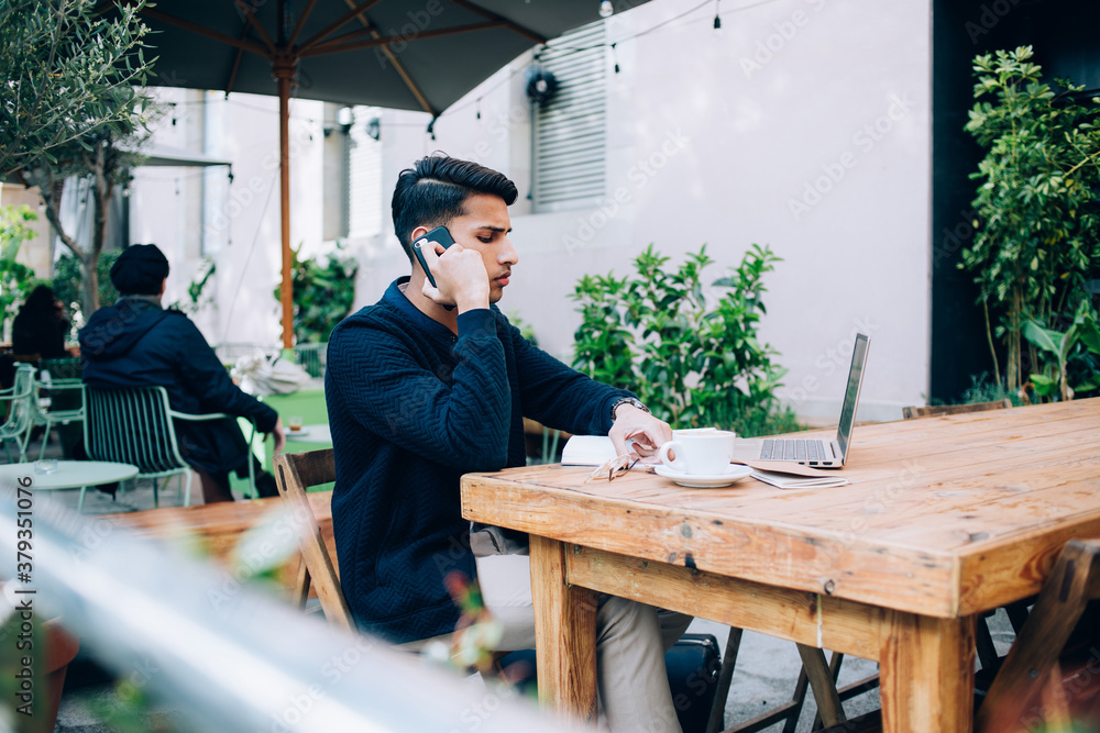 Fototapeta premium Pensive man talking on smartphone in street cafe