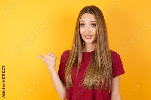 lovely Beautiful Young beautiful caucasian girl wearing red t-shirt over isolated yellow background pointing aside with forefinger, showing at copy space having news about bargains