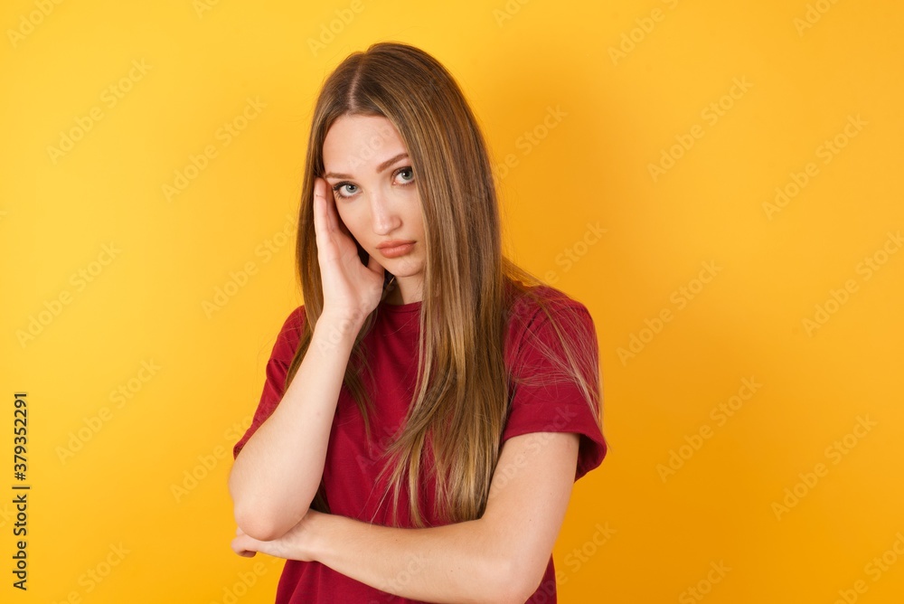 Very bored Beautiful Young beautiful caucasian girl wearing red t-shirt over isolated yellow background holding hand on cheek while support it with another crossed hand, looking tired and sick, Very bored Beautiful Young beautiful caucasian girl wearing red t-shirt over isolated yellow background holding hand on cheek while support it with another crossed hand, looking tired and sick,