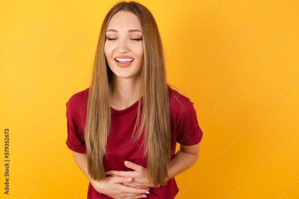 Beautiful Young beautiful caucasian girl wearing red t-shirt over isolated yellow background smiling and laughing hard out loud because funny crazy joke with hands on body. Beautiful Young beautiful caucasian girl wearing red t-shirt over isolated yellow background smiling and laughing hard out loud because funny crazy joke with hands on body.
