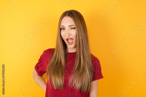 Beautiful Young beautiful caucasian girl wearing red t-shirt over isolated yellow background winking looking at the camera with sexy expression, cheerful and happy face.