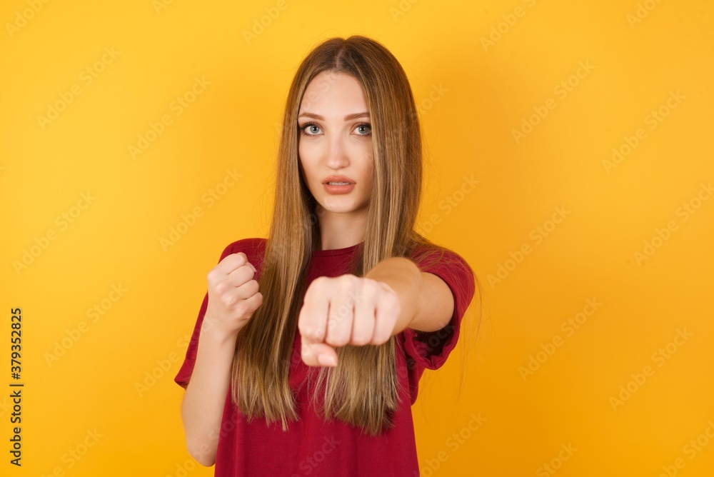 Beautiful Young beautiful caucasian girl wearing red t-shirt over isolated yellow background Punching fist to fight, aggressive and angry attack, threat and violence Beautiful Young beautiful caucasian girl wearing red t-shirt over isolated yellow background Punching fist to fight, aggressive and angry attack, threat and violence