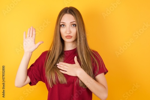 Beautiful Young beautiful caucasian girl wearing red t-shirt over isolated yellow background Swearing with hand on chest and open palm, making a loyalty promise oath
