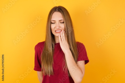 Beautiful Young beautiful caucasian girl wearing red t-shirt over isolated yellow background touching mouth with hand with painful expression because of toothache or dental illness on teeth.