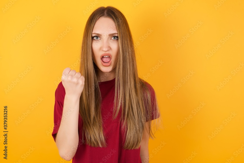 Beautiful Young beautiful caucasian girl wearing red t-shirt over isolated yellow wall being angry and mad raising fist frustrated and furious while shouting with anger. Rage and aggressive concept. Beautiful Young beautiful caucasian girl wearing red t-shirt over isolated yellow wall being angry and mad raising fist frustrated and furious while shouting with anger. Rage and aggressive concept.