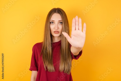 Beautiful Young beautiful caucasian girl wearing red t-shirt over isolated yellow background doing stop gesture with palm of the hand. Warning expression with negative and serious gesture on the face