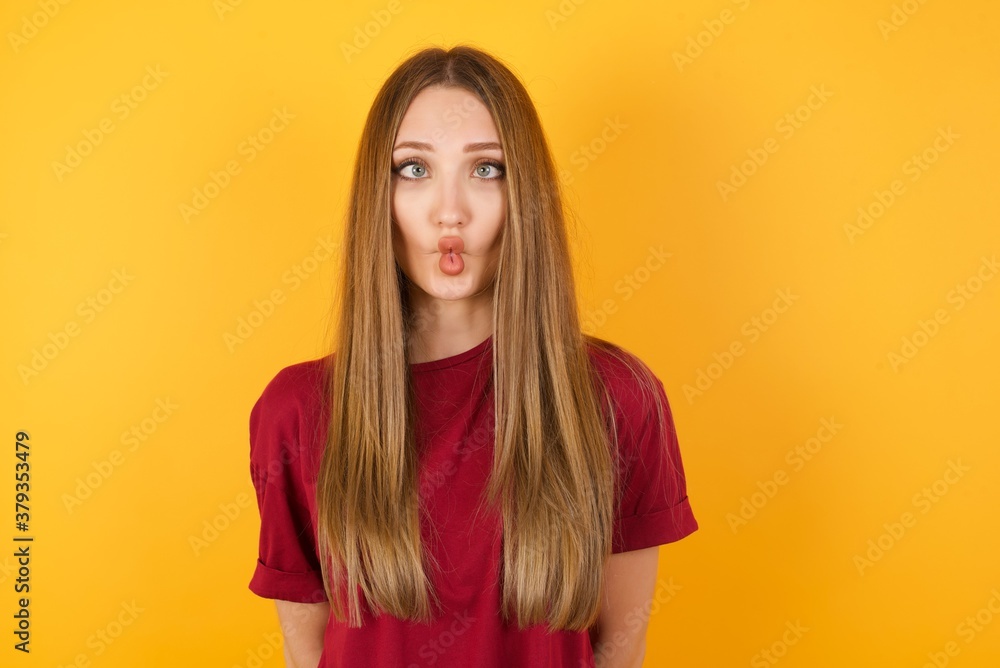 Beautiful Young beautiful caucasian girl wearing red t-shirt over isolated yellow background making fish face with lips, crazy and comical gesture. Funny expression. Beautiful Young beautiful caucasian girl wearing red t-shirt over isolated yellow background making fish face with lips, crazy and comical gesture. Funny expression.
