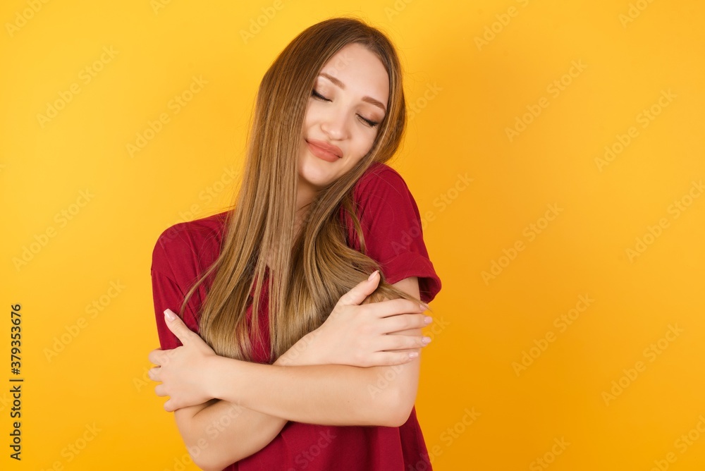 Obraz premium Beautiful Young beautiful caucasian girl wearing red t-shirt over isolated yellow background Hugging oneself happy and positive, smiling confident. Self love and self care