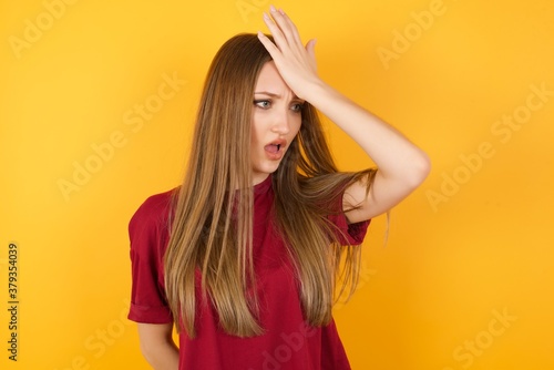 Beautiful Young beautiful caucasian girl wearing red t-shirt over isolated yellow background surprised with hand on head for mistake, remember error. Forgot, bad memory concept.
