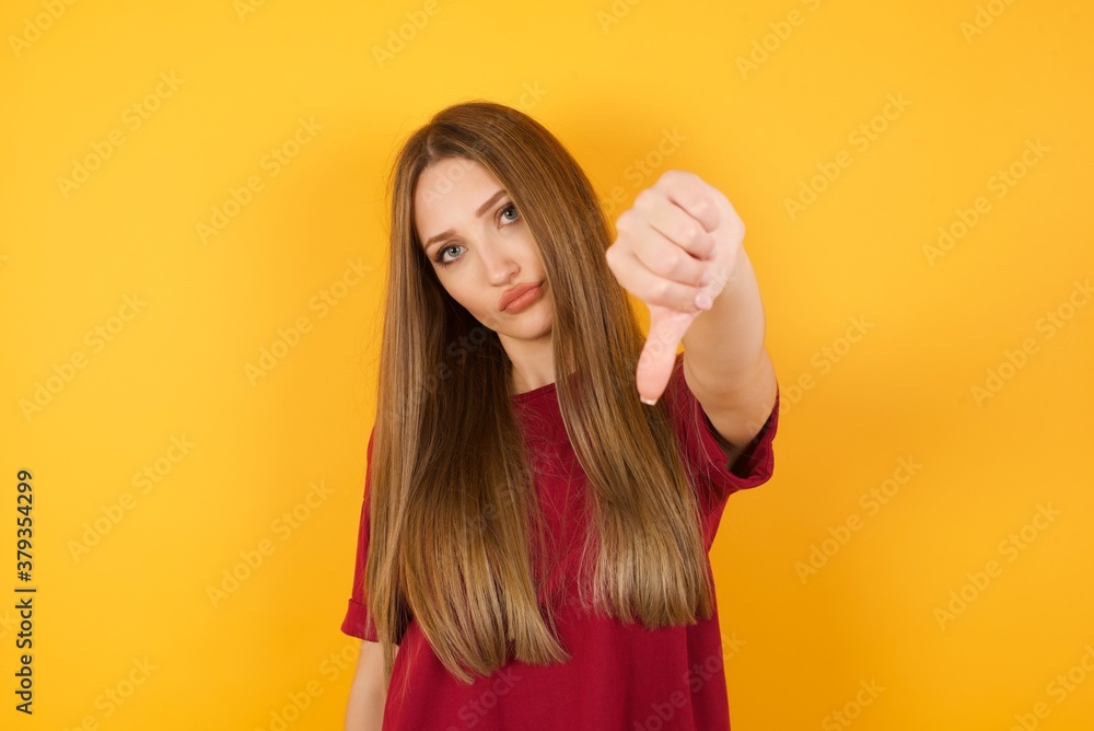 Beautiful Young beautiful caucasian girl wearing red t-shirt over isolated yellow wall feeling angry, annoyed, disappointed or displeased, showing thumbs down with a serious look against white wall Beautiful Young beautiful caucasian girl wearing red t-shirt over isolated yellow wall feeling angry, annoyed, disappointed or displeased, showing thumbs down with a serious look against white wall