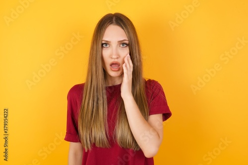 Beautiful Young beautiful caucasian girl wearing red t-shirt over isolated yellow wall looks with great surprisment being very stunned, astonished with unexpected news, . Facial expressions concept.