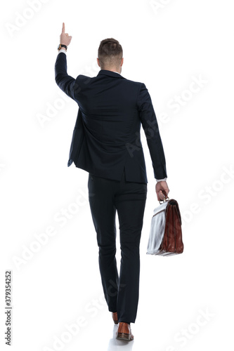 Back view of businessman holding briefcase and pointing up
