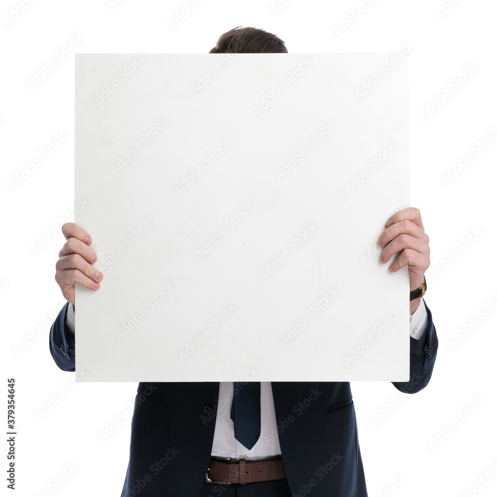 Young businessman covering his face with blank billboard Young businessman covering his face with blank billboard