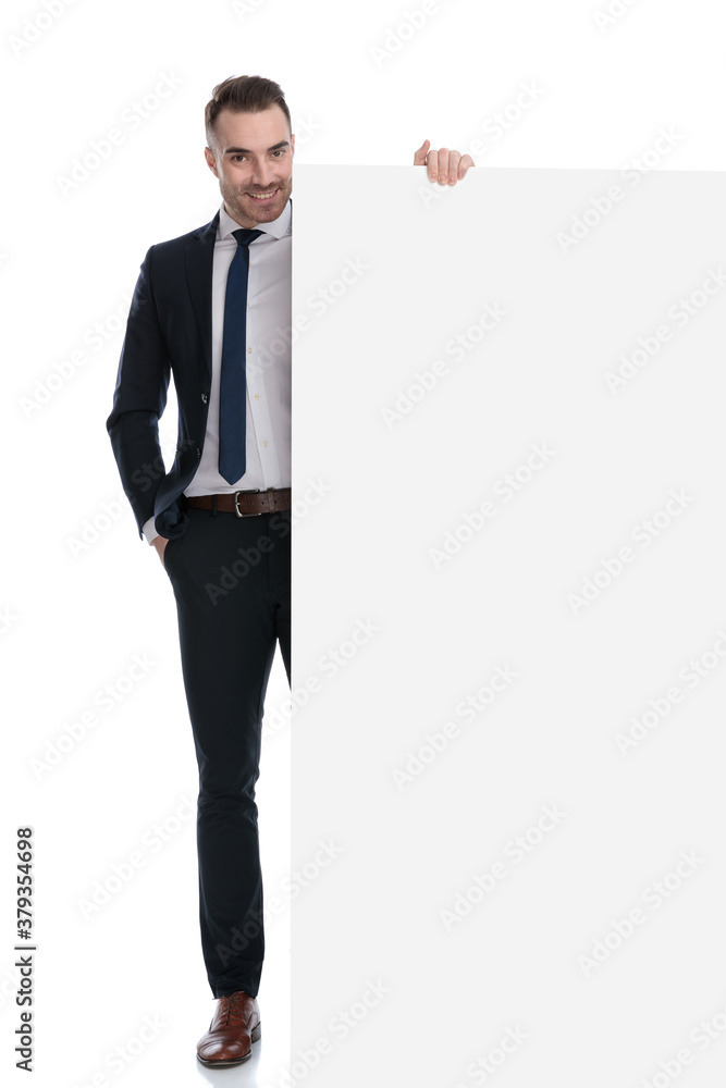 Smiling businessman presenting empty billboard and holding hand in pocket