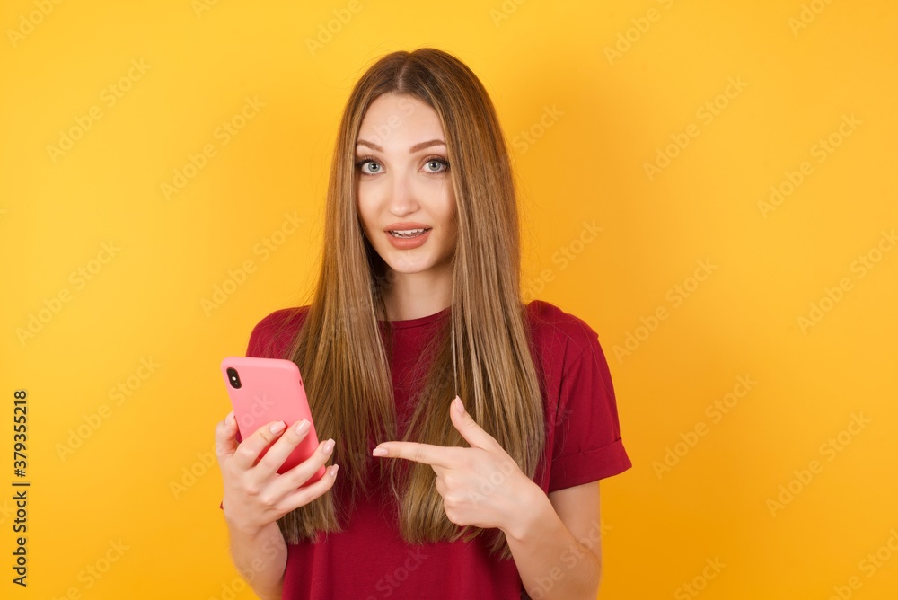 Beautiful Young beautiful caucasian girl wearing red t-shirt over isolated yellow background holding in hands showing new cell, Beautiful Young beautiful caucasian girl wearing red t-shirt over isolated yellow background holding in hands showing new cell,
