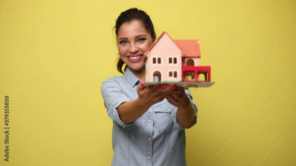happy young casual woman in blue denim shirt presenting and recommending building model, smiling and nodding on yellow background happy young casual woman in blue denim shirt presenting and recommending building model, smiling and nodding on yellow background