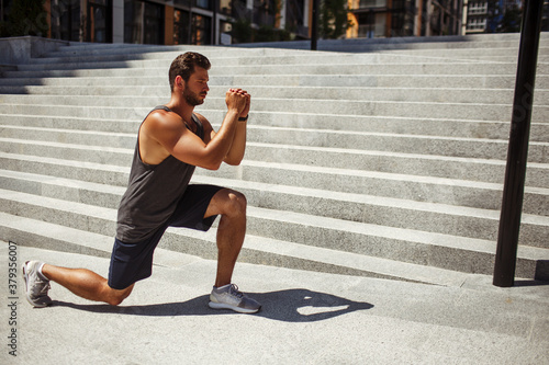 Young man exercising outside. Strong powerful guy stand on one knee and hold hands in front himself. Doing one leg squat exercise. Training his body and muscles.