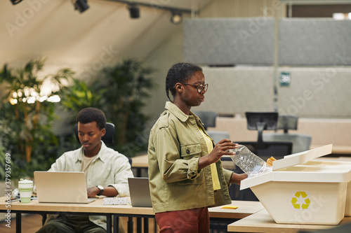 Fotografie Side view portrait of young African-American woman putting paper cup into waste