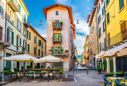 Traditional colorful building with balconies and shutter windows in typical italian street, tables and tent of street restaurant, Brescia city historical centre, Lombardy, Northern Italy © Aliaksandr