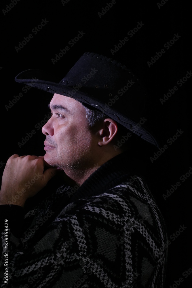 Portrait of wise thoughtful man in black hat sitting sideways and holding his chin with hand isolated on black background Portrait of wise thoughtful man in black hat sitting sideways and holding his chin with hand isolated on black background