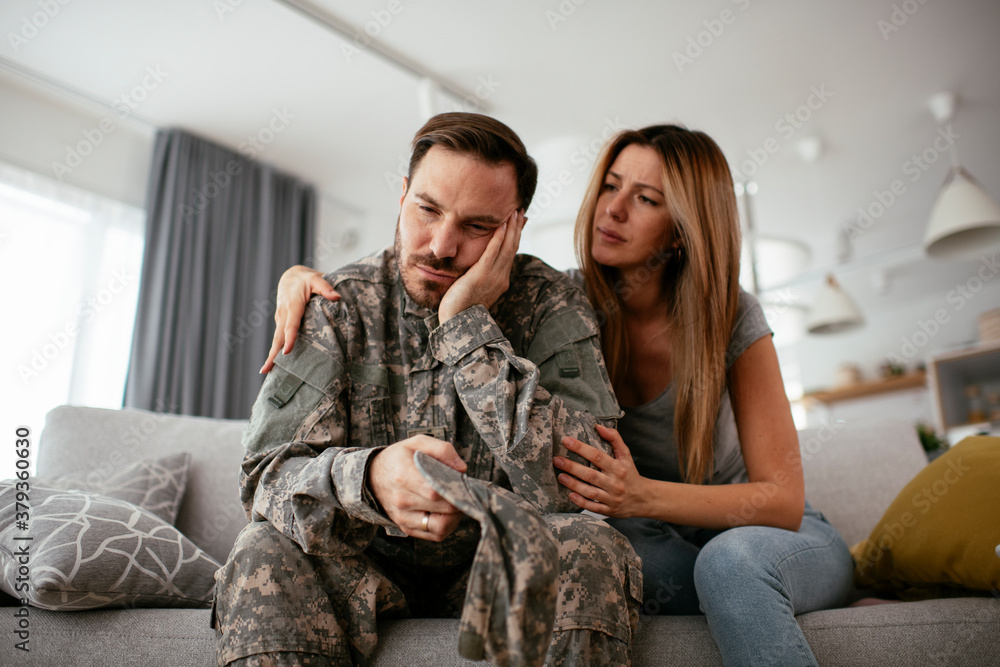 Depressed soldier sitting on sofa with his wife. Young marine having PTSD..