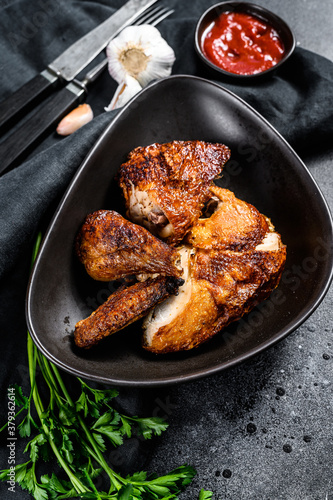 Half a grilled chicken on a plate. Black background. Top view