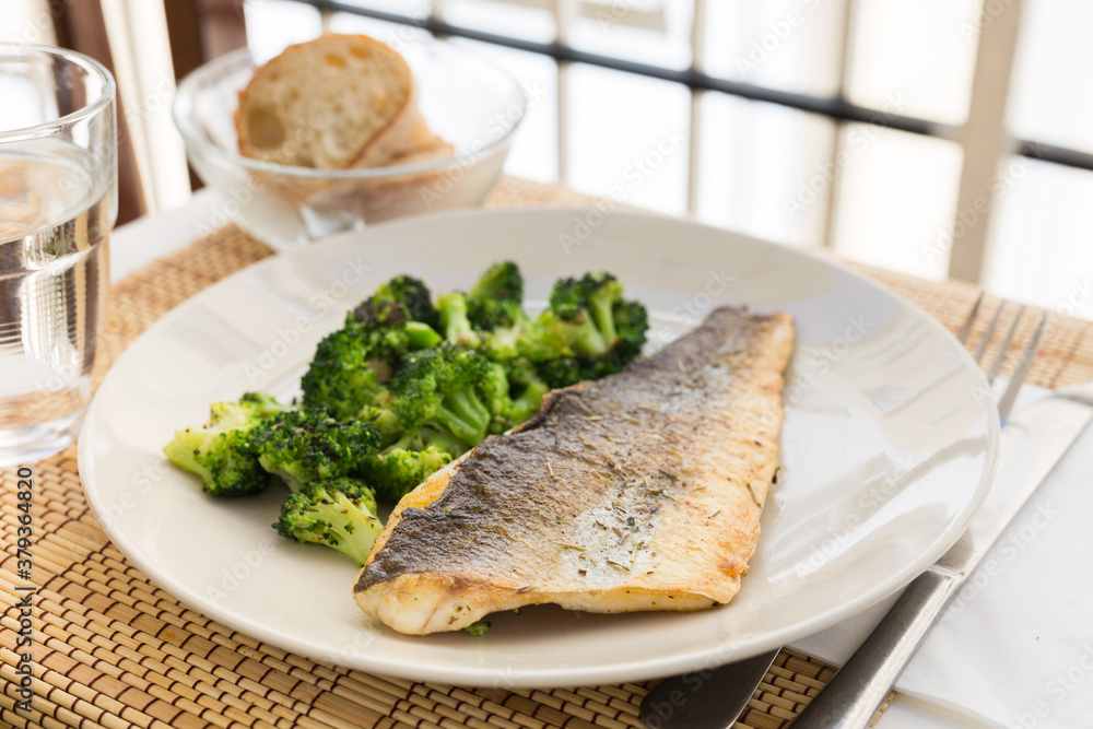 fried fillet of sea bass with garnish of broccoli on black warm stone plate fried fillet of sea bass with garnish of broccoli on black warm stone plate
