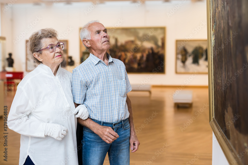 Fototapeta premium mature European couple examines paintings in an exhibition in hall of art museum