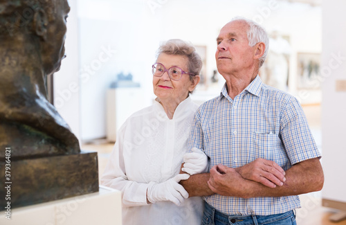 mature European couple examines paintings in an exhibition in hall of art museum