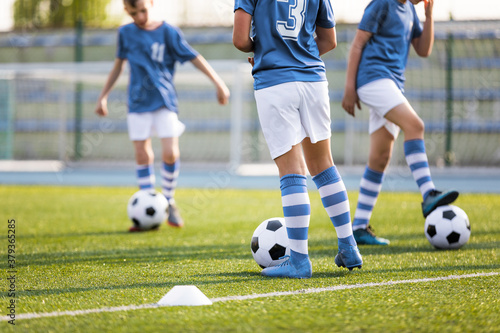 Fototapeta Naklejka Na Ścianę i Meble -  Legs of Boys Soccer Players on Grass Training Venue. Kids in Light Blue Shirts Kicking Soccer Balls. School Soccer Training Class