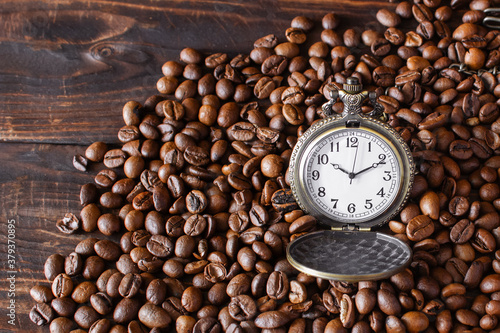 Vintage opened pocket watch among coffee beans on brown wooden table. Morning coffee,10 o'clock.