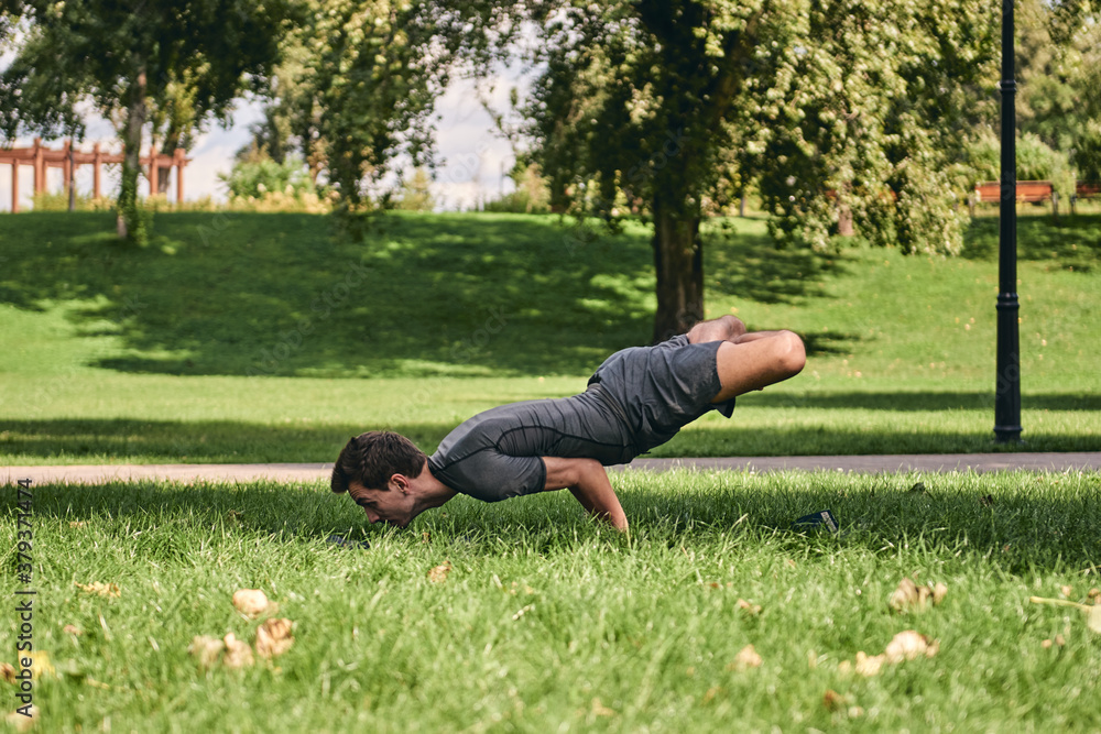 Young athletic man in sportswear doing yoga in the park. Practice asana outdoors. People exercising on green grass with yoga mat. Strong mature caucasian man in difficult lotus peacock pose Young athletic man in sportswear doing yoga in the park. Practice asana outdoors. People exercising on green grass with yoga mat. Strong mature caucasian man in difficult lotus peacock pose