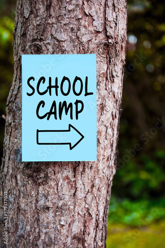 School camp sign with an arrow written on paper mounted on a tree in the forest. Outdoor education.