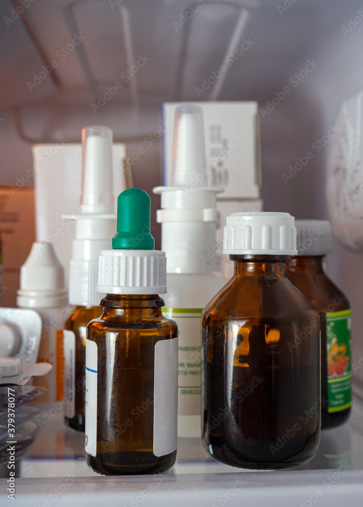 Herbal tincture vials, nosal sprays, eye drops and boxes on the refrigerator shelf close-up. Medical background with medicines. Herbal tincture vials, nosal sprays, eye drops and boxes on the refrigerator shelf close-up. Medical background with medicines.