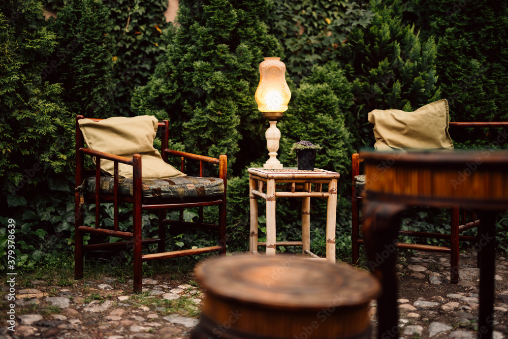 Cozy garden in the evening. Wooden rustic table, armchair and vintage lamp in lovely garden. Cozy garden in the evening. Wooden rustic table, armchair and vintage lamp in lovely garden.