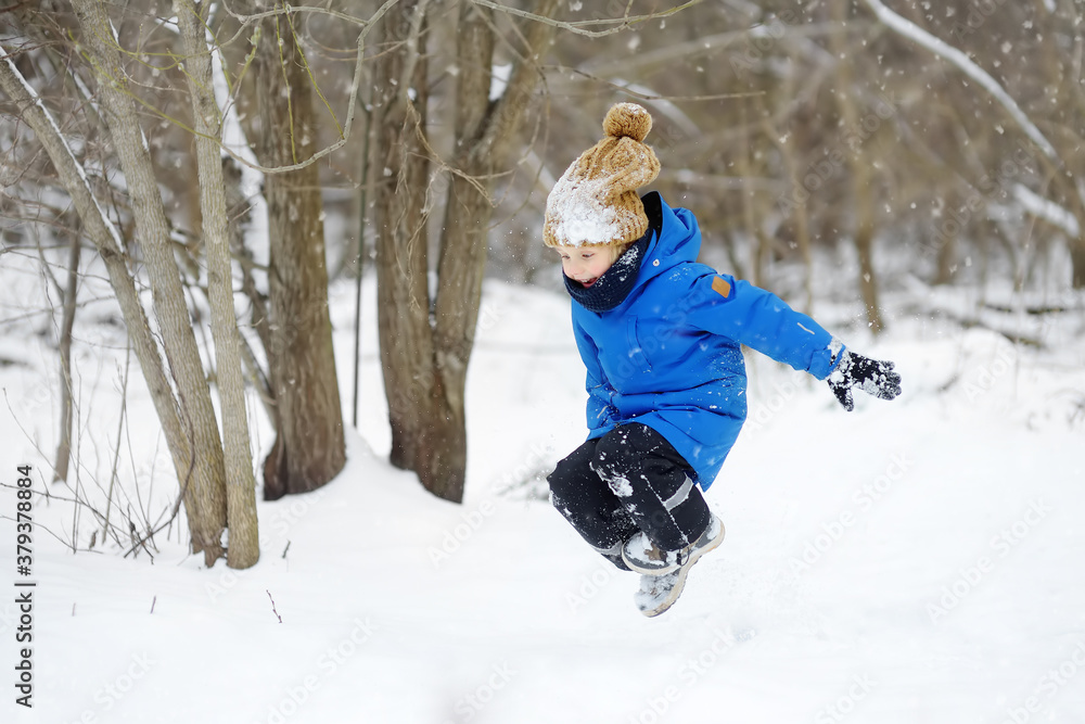 Little boy jumping in snowdrift and having fun playing with fresh snow. Active outdoors leisure for child in snowy winter day.