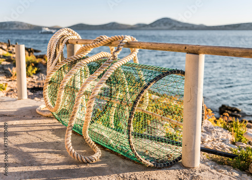 Cylindrical fish trap with ropes drying on the shore near the village at sunset photo