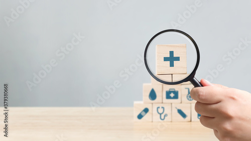 Hand holding magnifying glass to wood block stacking with icon healthcare medical, Insurance for your health concept photo