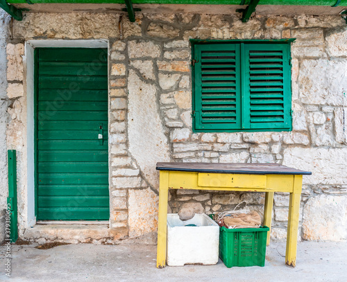 Yellow table, green door and window on the wall of sandstone in the village of Lavsa, Croatia photo